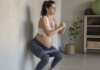 Ni reposo absoluto ni promesas milagrosas: qué puede hacer de verdad el entrenamiento de fuerza contra la diabetes del embarazo Mujer embarazada en estudio, cerca de pared, realiza sentadilla asistida con banda elÔstica; composición lateral, plano medio